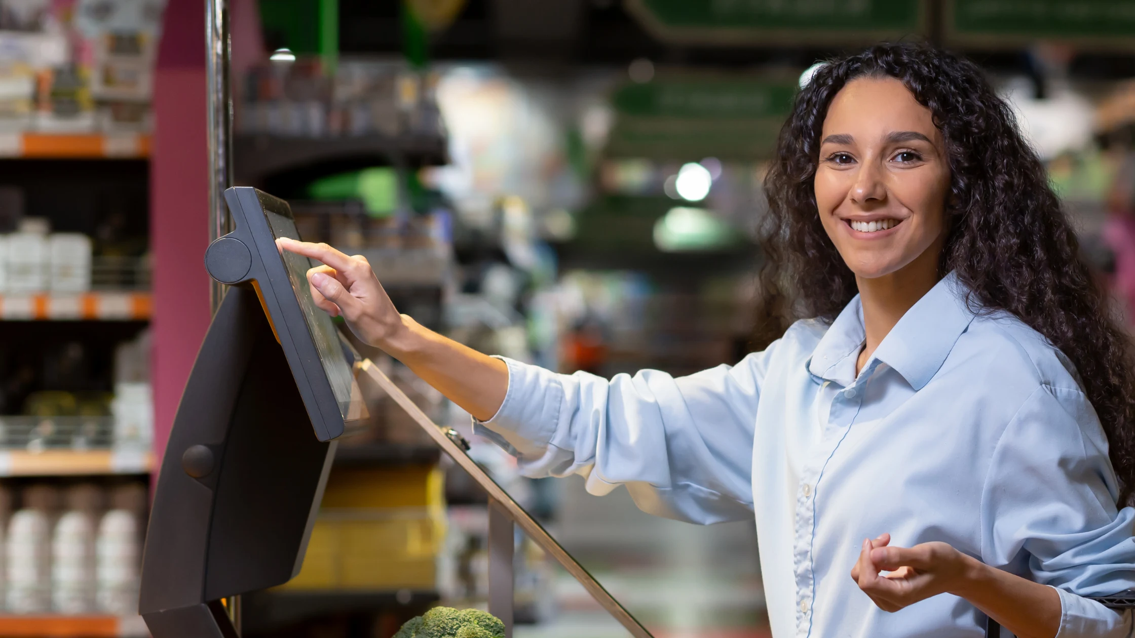 Smiling woman tapping a checkout screen at a grocery store, representing the Round Up at the Register donation program at Kimberton Whole Foods Wyomissing
