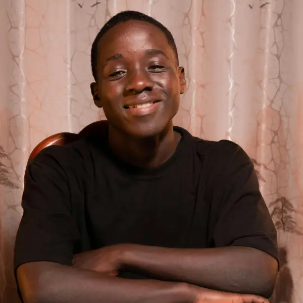 A smiling young boy sits with arms crossed at a table indoors, representing a youth participant in the Family Promise of Berks County U-Turn Program.